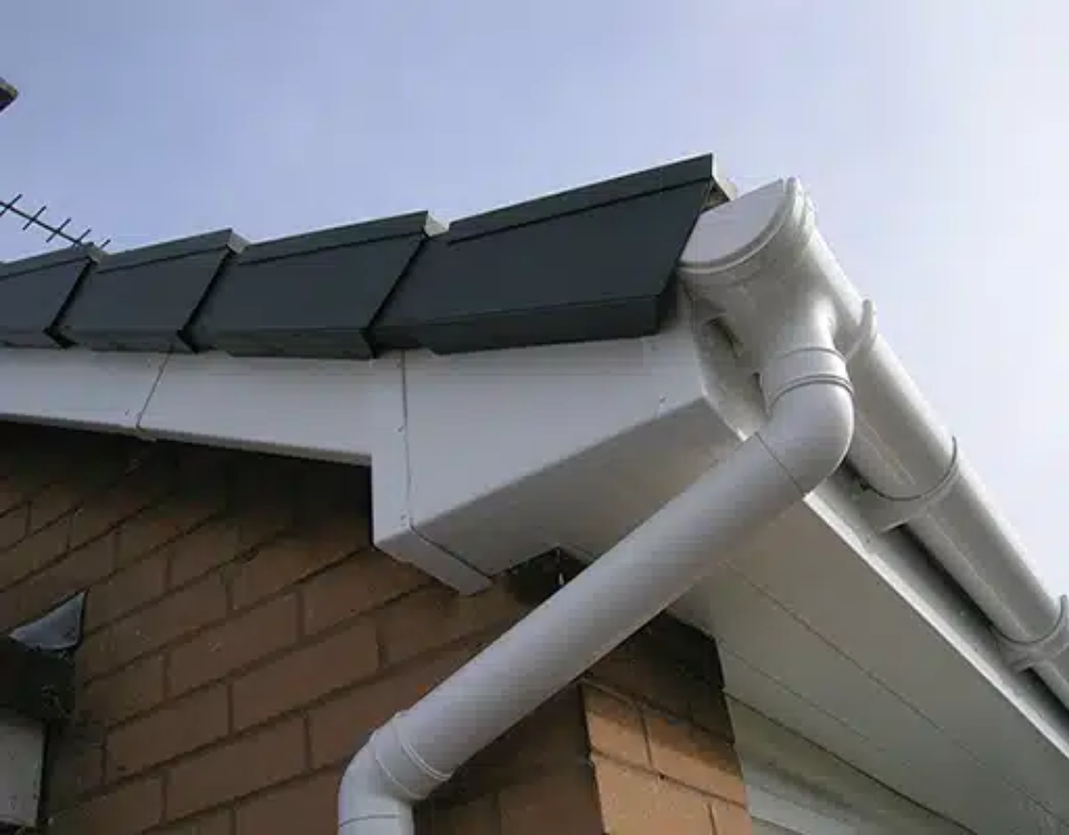 White gutter and downspout on a house roof with green trim and brick exterior