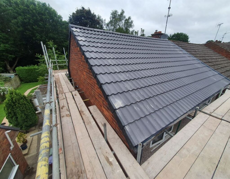 Roofers working on a house roof with gray tiles and wooden scaffolding beside red brick walls