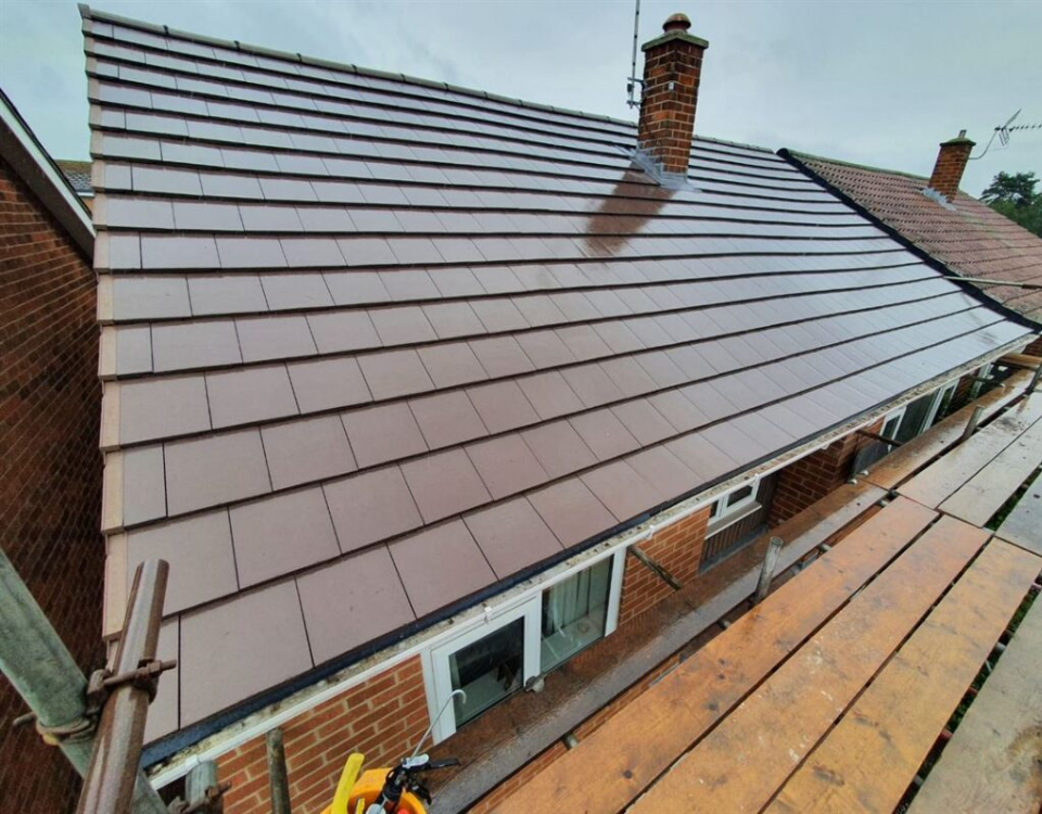 Roofing work on a steep house roof with brown metal panels and a brick chimney