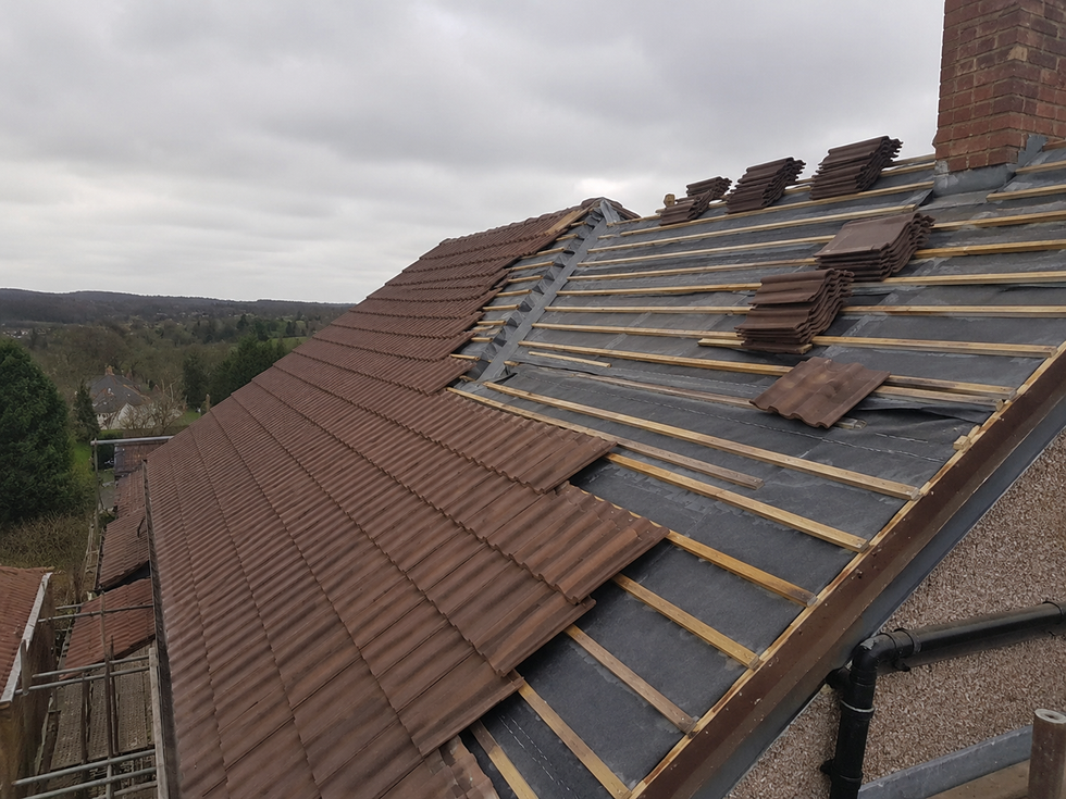 Partially roofed house with exposed underlayment and stacked brown roof tiles during repair