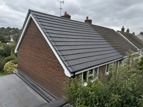 Brick house with dark gray tiled roof and white trim, seen from above with nearby greenery