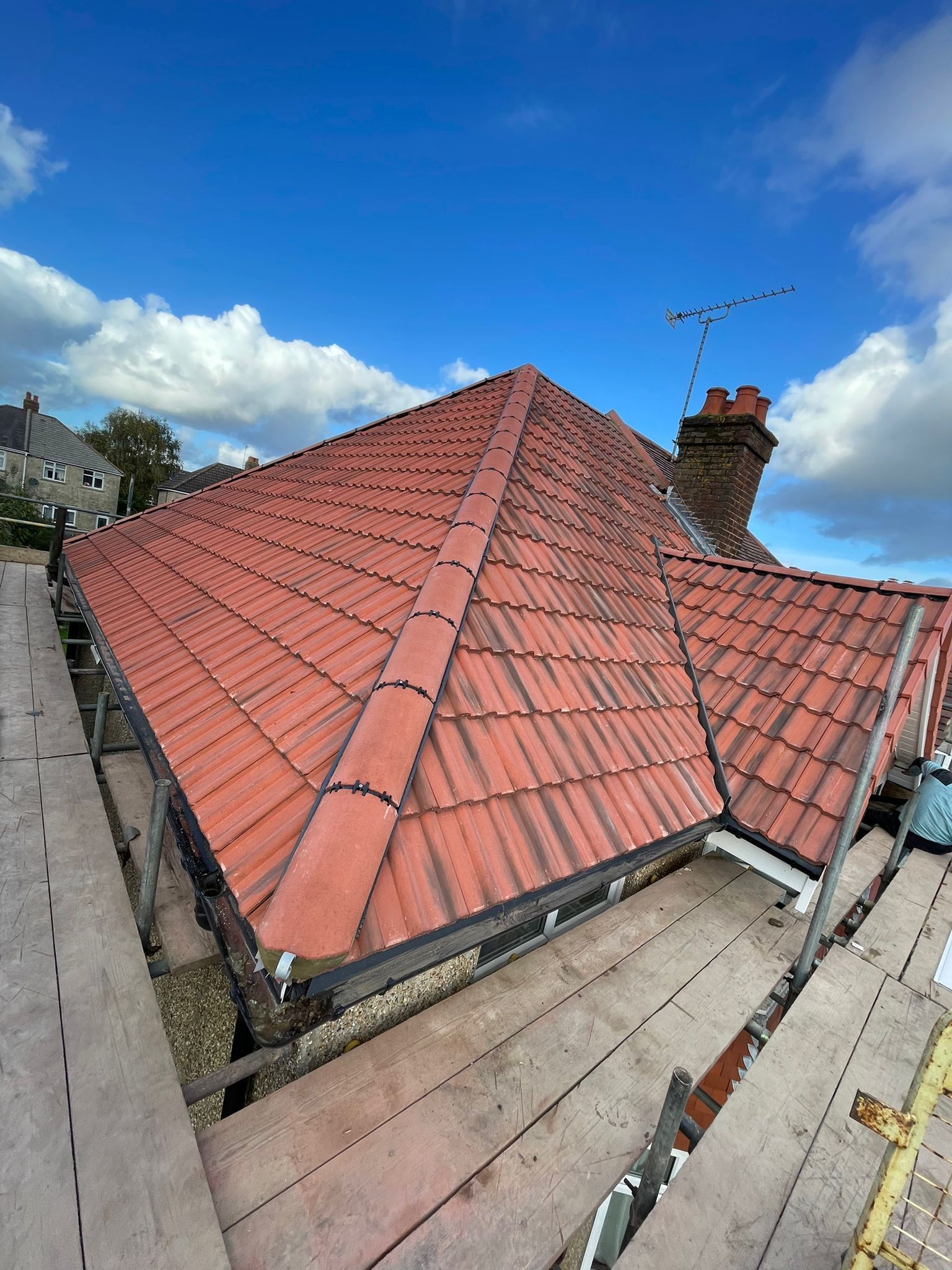 Red tiled rooftop with chimney under a blue sky and clouds