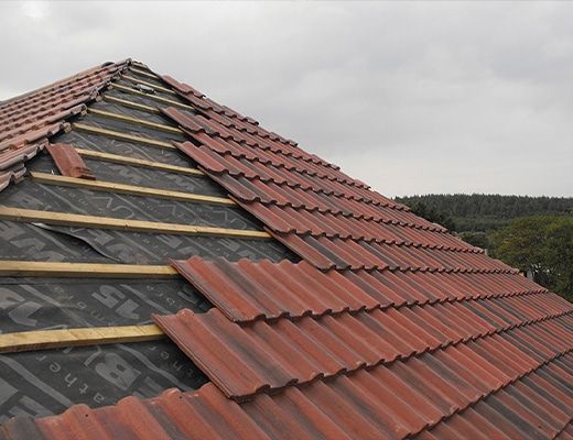 Roof under construction with red tiles and exposed underlayment on a cloudy day