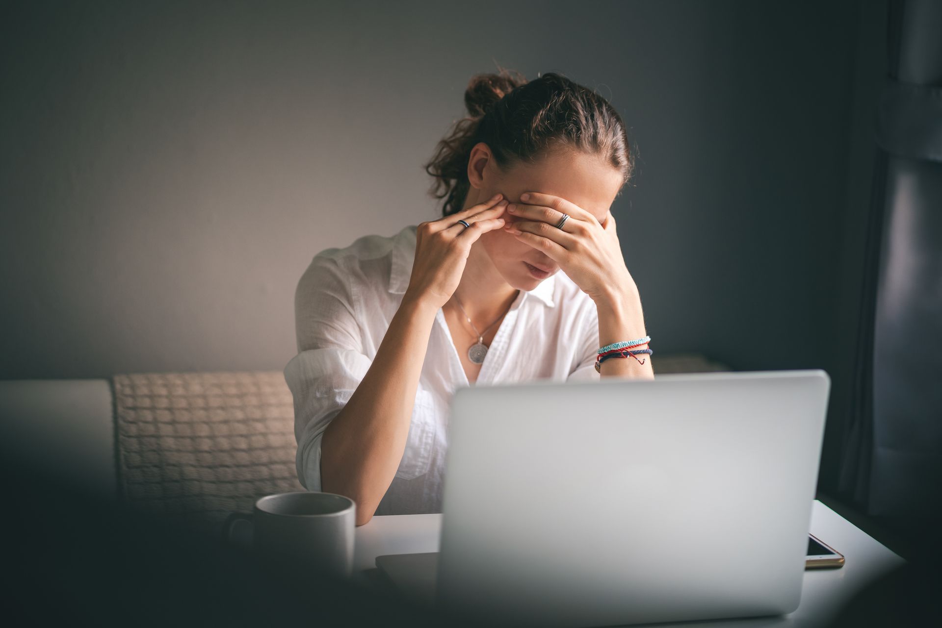 Pessoa estressada em frente a um laptop, com a cabeça entre as mãos, em um quarto pouco iluminado.