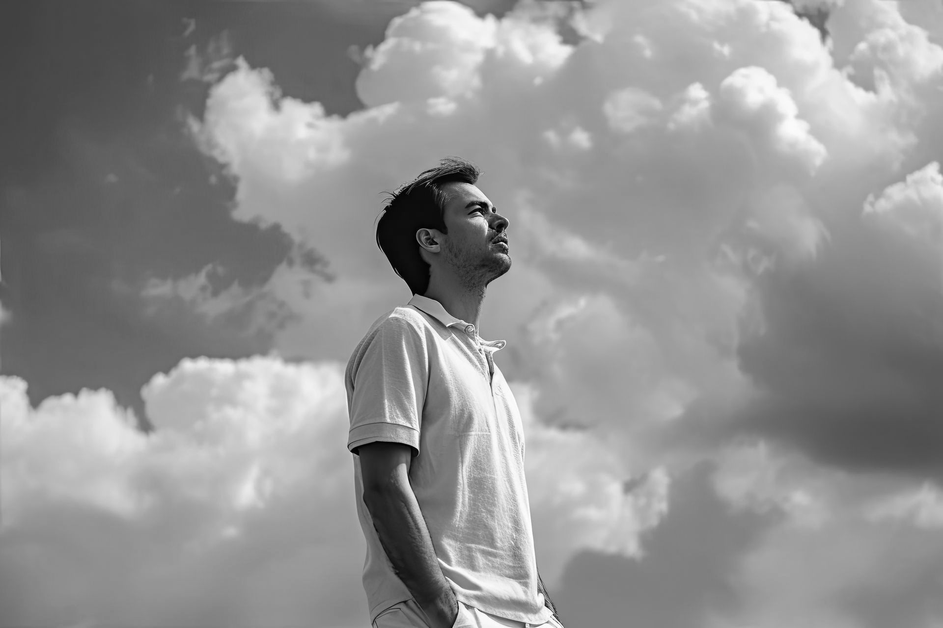 Homem de perfil, vestindo uma camiseta branca, olhando para cima sob um céu nublado.