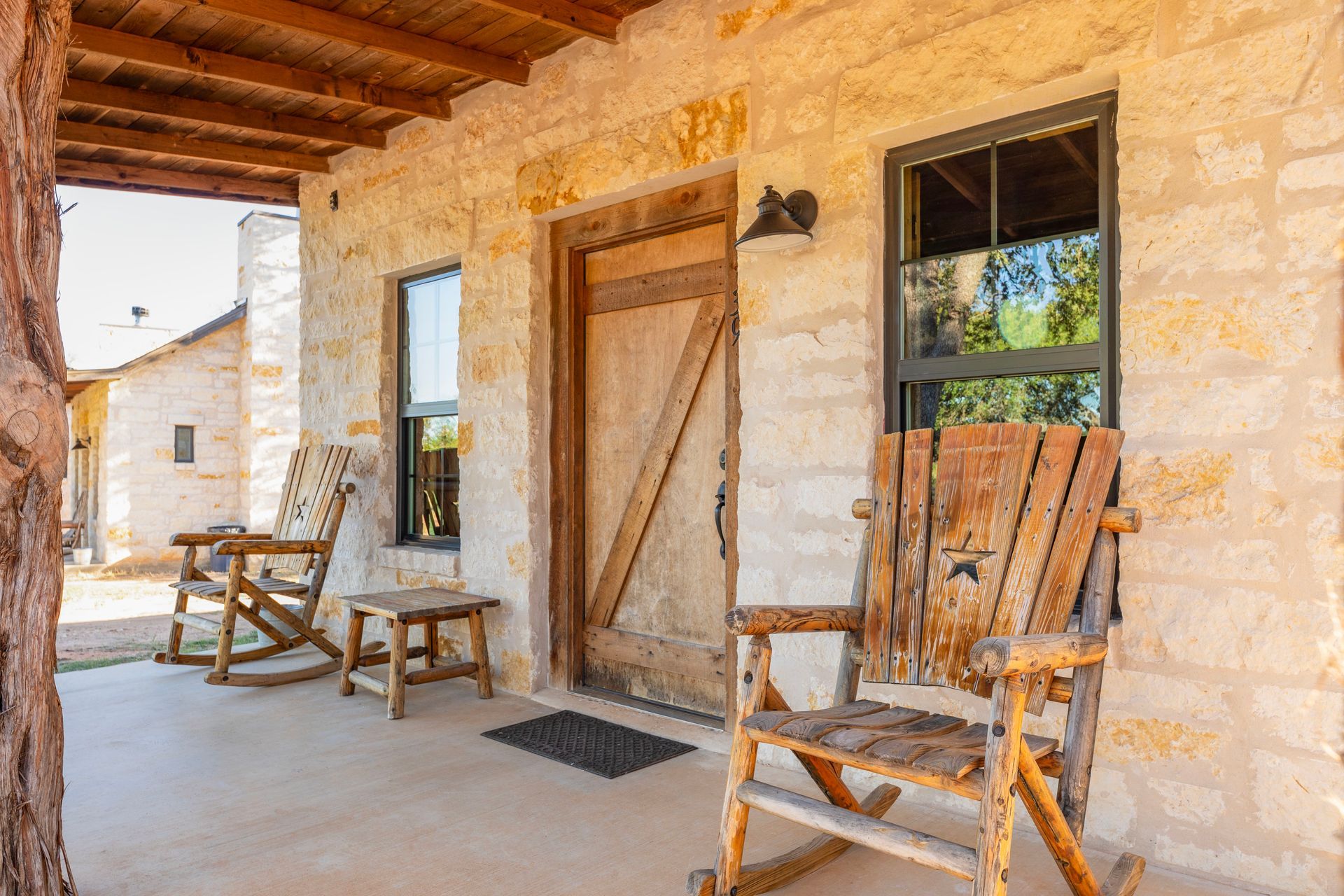 Stone house porch with rocking chairs, wooden door, and windows.