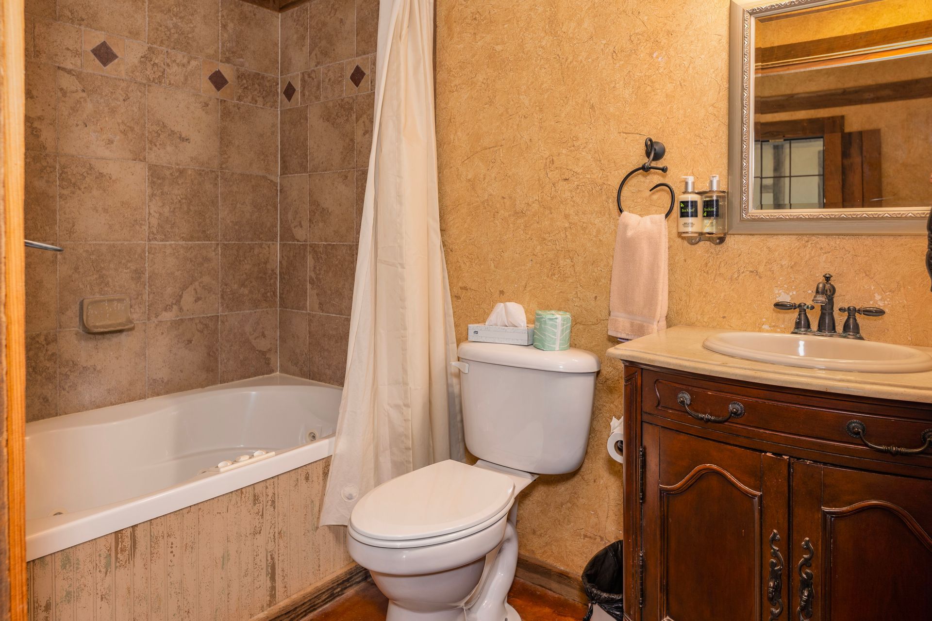 Bathroom with bathtub, toilet, sink, and vanity; earth tone walls, tiled bathtub surround.