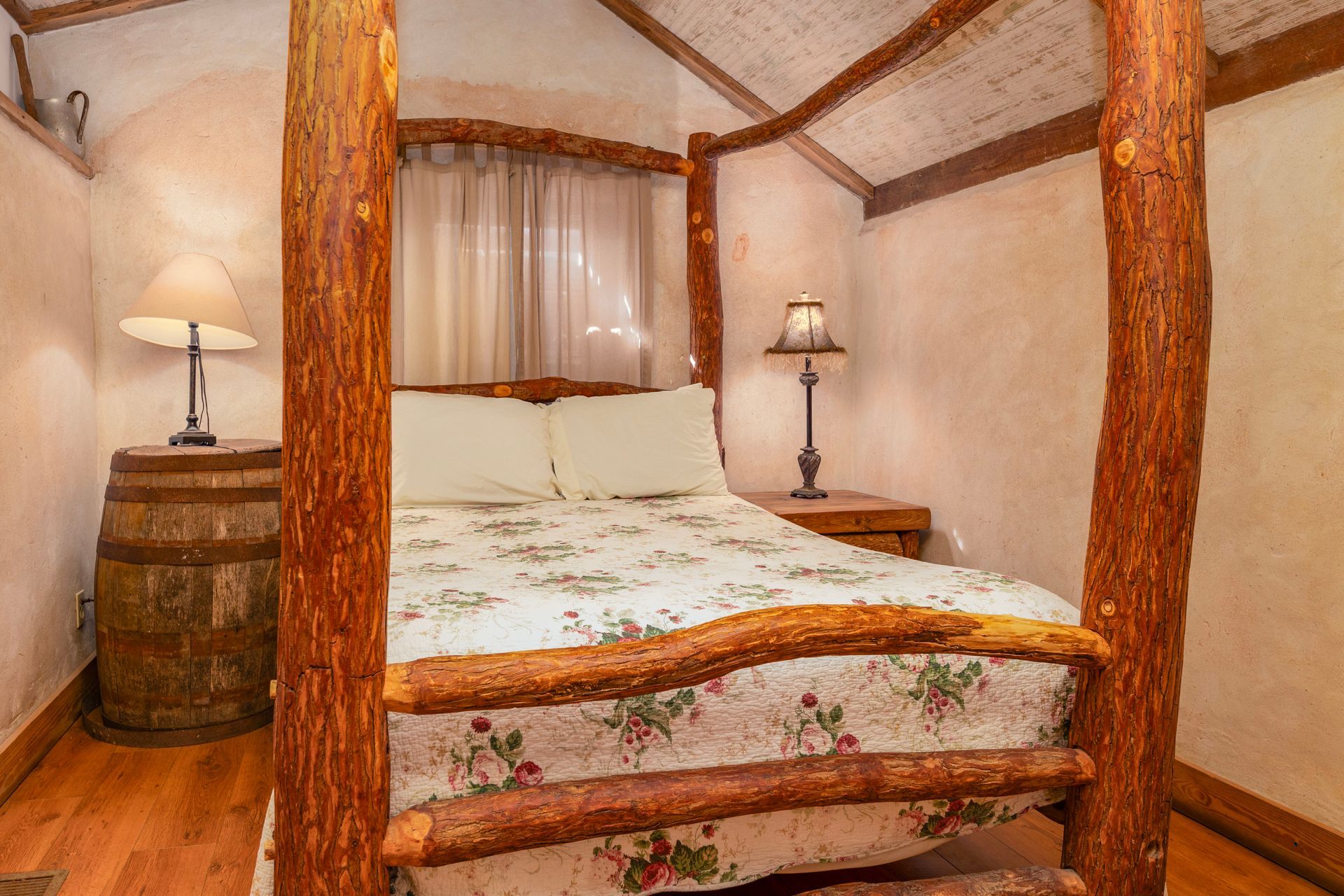 Cozy bedroom with log bed frame, quilt, lamp on barrel and nightstand.