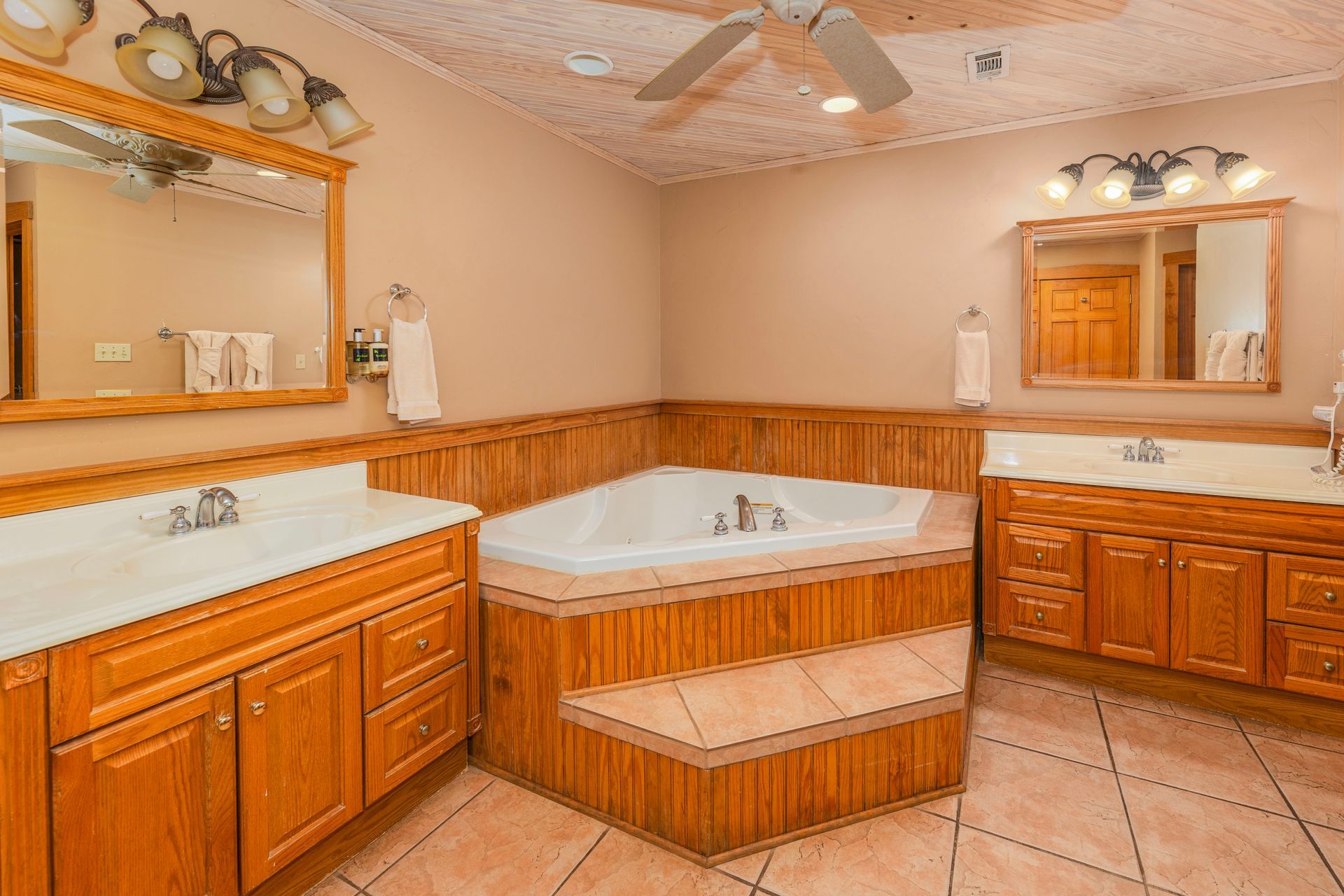 Bathroom with a jacuzzi, two sinks, and wooden cabinets.