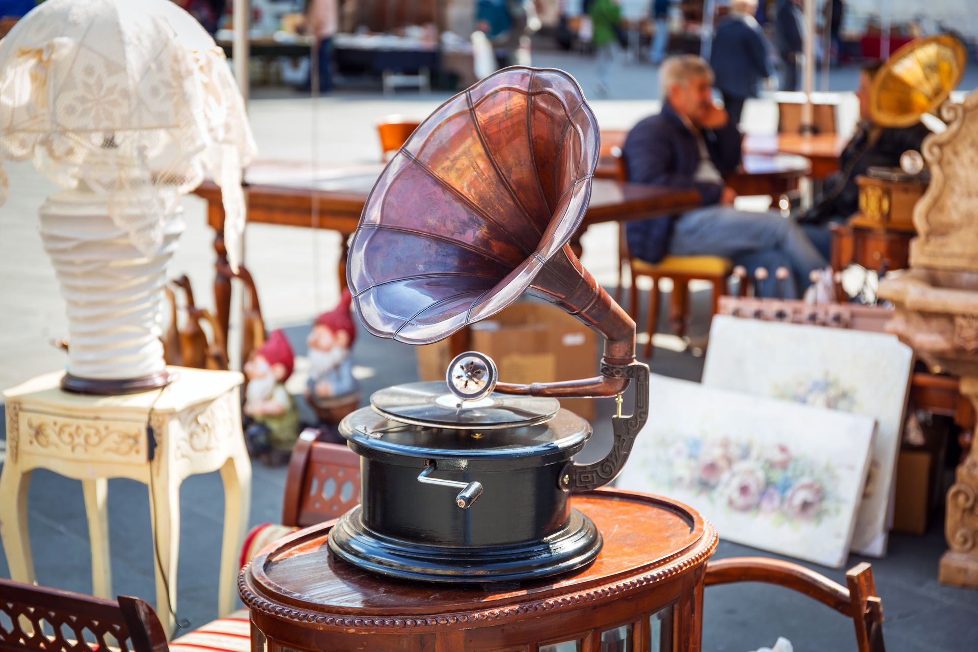 A vintage phonograph with a large, dark horn sits on a wooden table at an outdoor antique market.