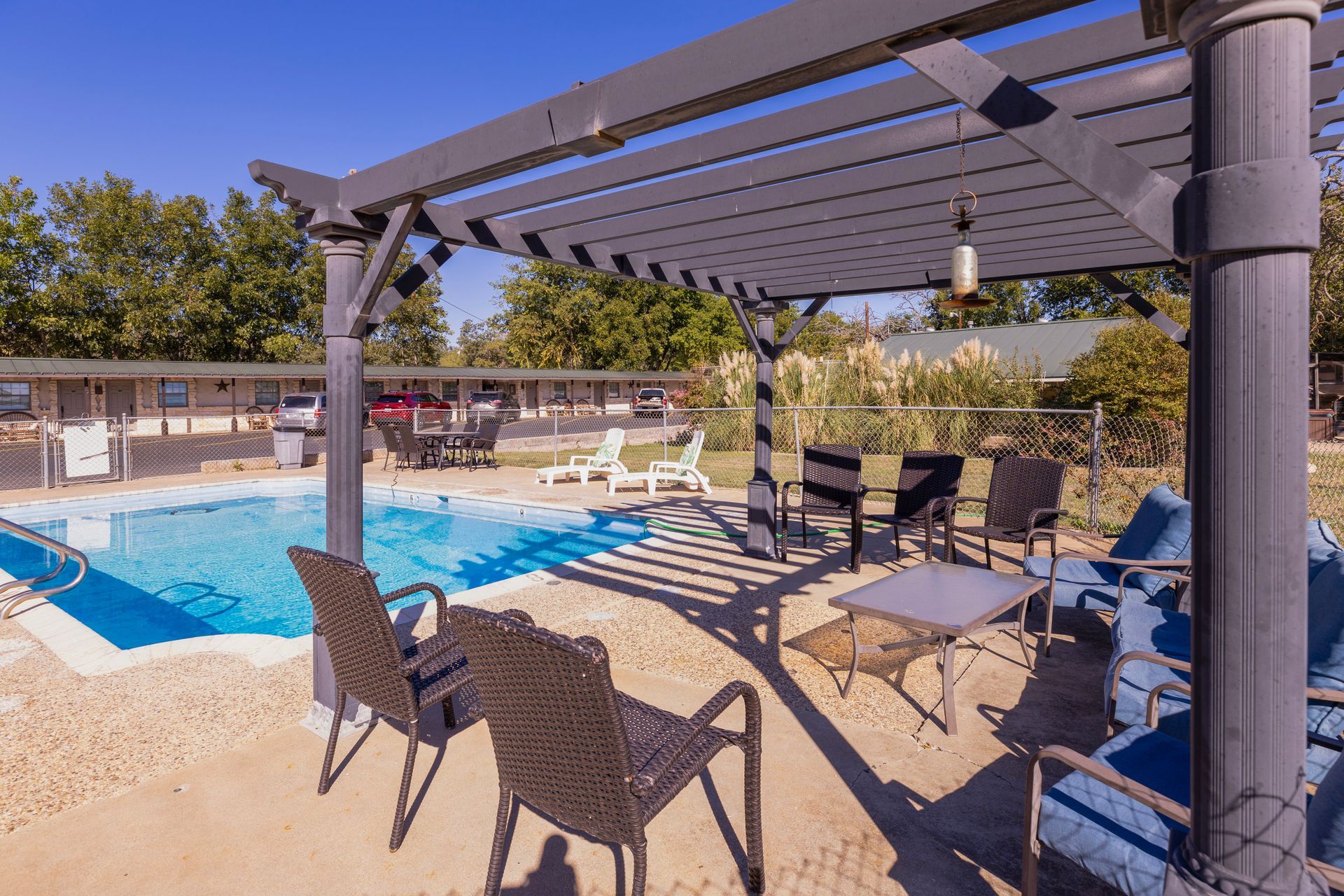 Poolside patio with pergola, chairs, and pool in background.