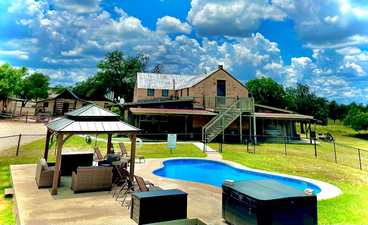 House with a pool, gazebo, and outdoor seating under a cloudy blue sky.