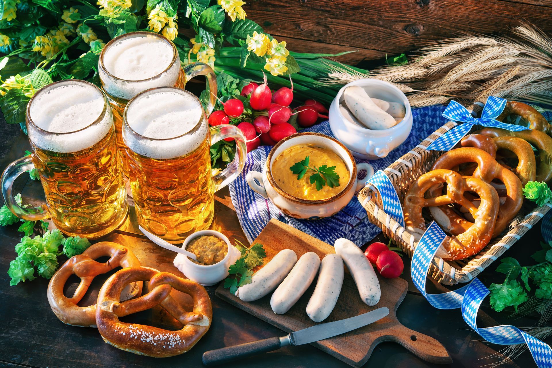 Four beers, pretzels, sausages, mustard, and dip. Bavarian food spread on a table.
