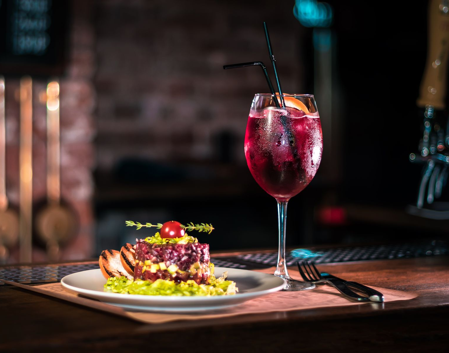 A plate with a stacked food dish and a red cocktail with a straw at a bar.