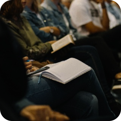 Um grupo de pessoas está sentado em uma fileira segurando livros e cadernos