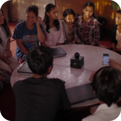 Um grupo de pessoas sentadas ao redor de uma mesa com um homem segurando um telefone celular