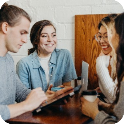 Um grupo de pessoas está sentado ao redor de uma mesa conversando e sorrindo.