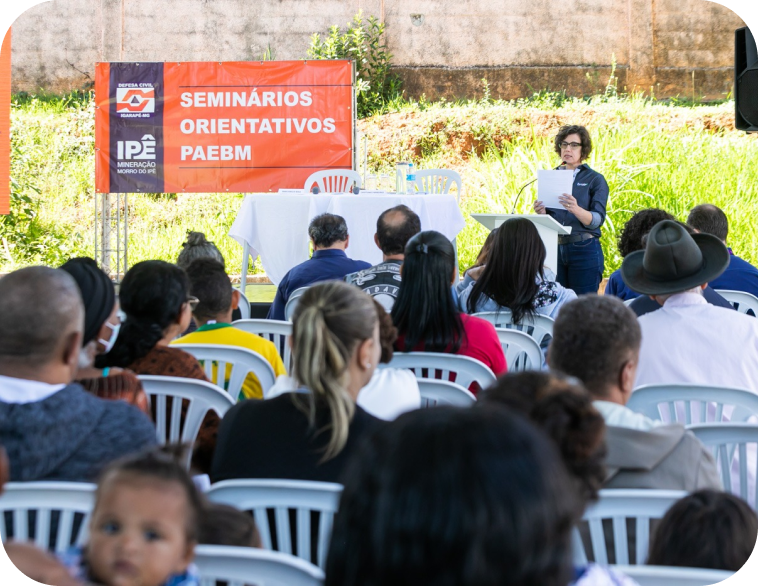 Uma mulher está fazendo uma apresentação para um grupo de pessoas em frente a uma placa que diz seminários orientativos paebm