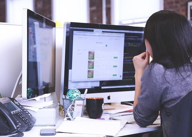 Uma mulher está sentada em uma mesa olhando para uma tela de computador.