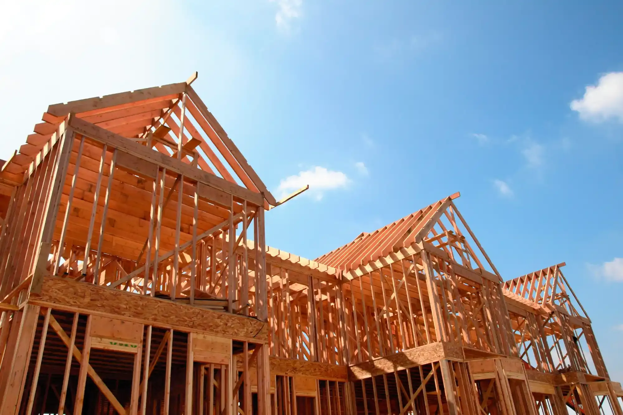 Wooden house frames under construction against a bright blue sky