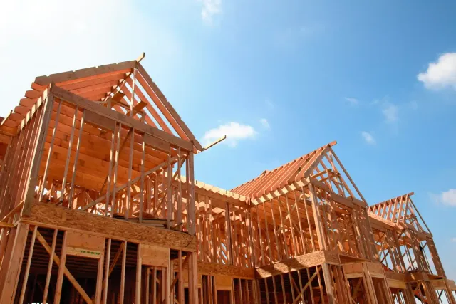 Wooden house frames under construction against a bright blue sky