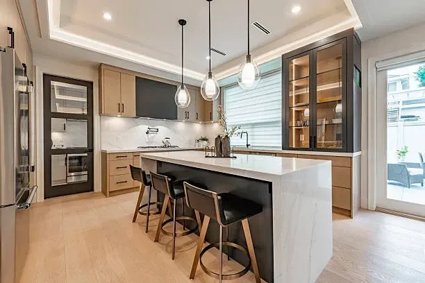 Modern kitchen with white island, black bar stools, wood cabinets, and pendant lights