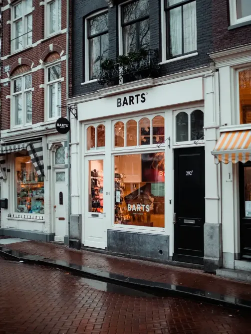 Storefront for BARTS on a rainy brick street, with white-framed windows and an orange awning.