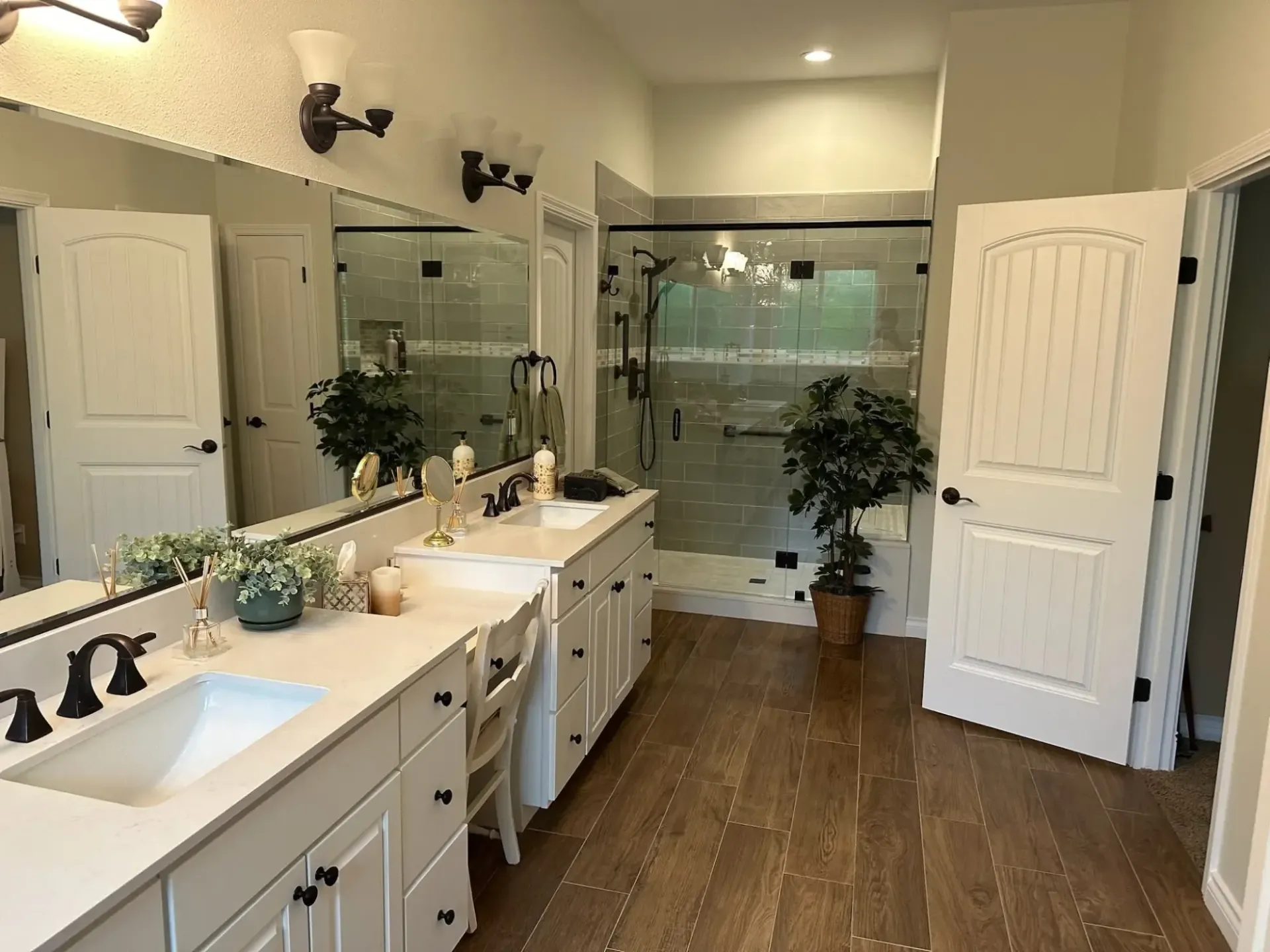 Bright bathroom with double vanity, large mirror, glass shower, and open doors.