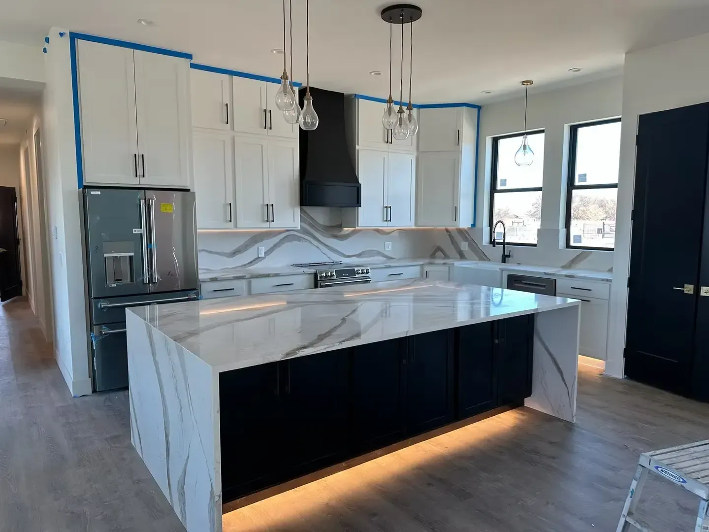 Modern white kitchen with marble island, black accents, stainless fridge, and pendant lights