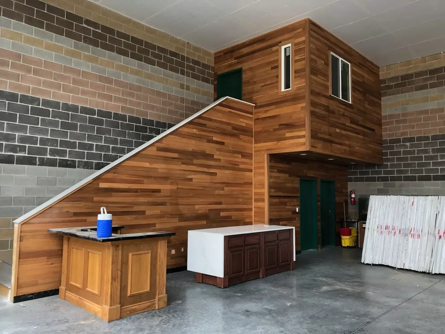 Wood-paneled staircase leading to a loft in an unfinished room with a concrete floor and storage cabinets