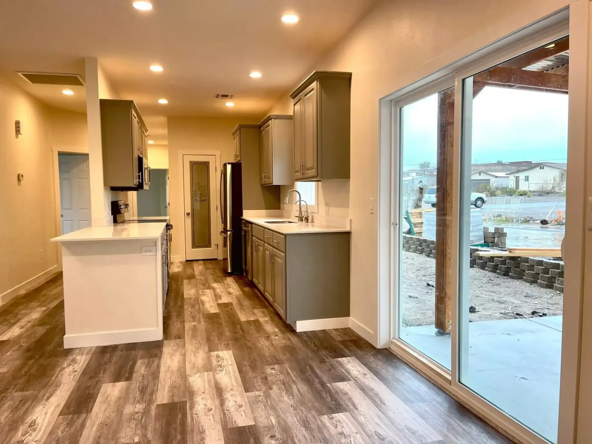 Empty modern kitchen and living space with wood floors and sliding glass doors to a patio.