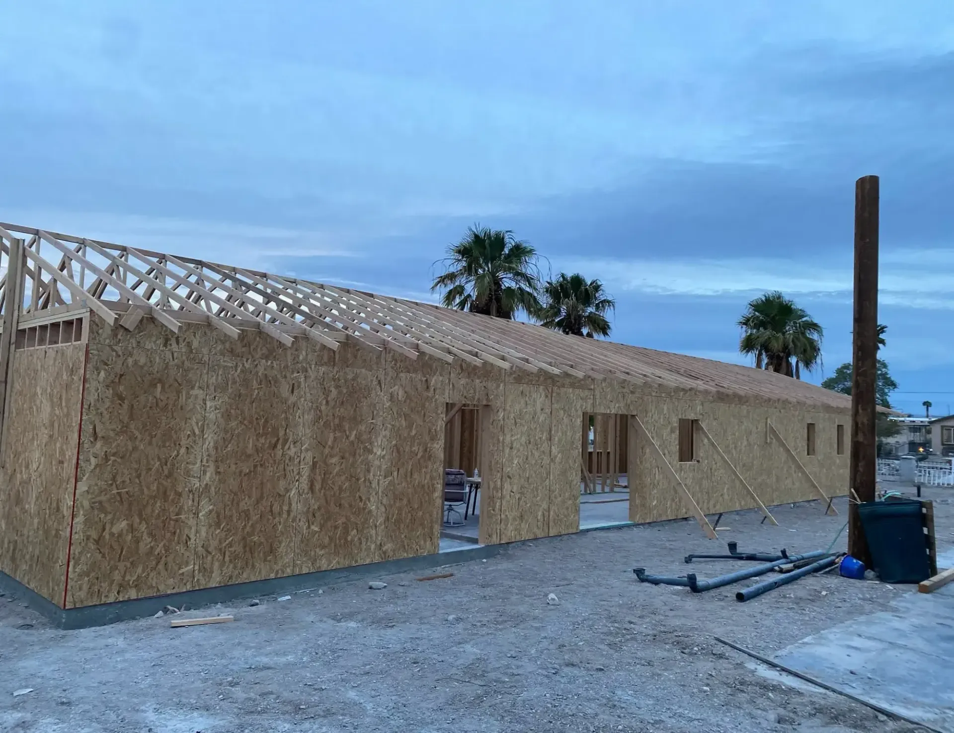 Partially built wooden house with truss framing under a cloudy blue sky at dusk