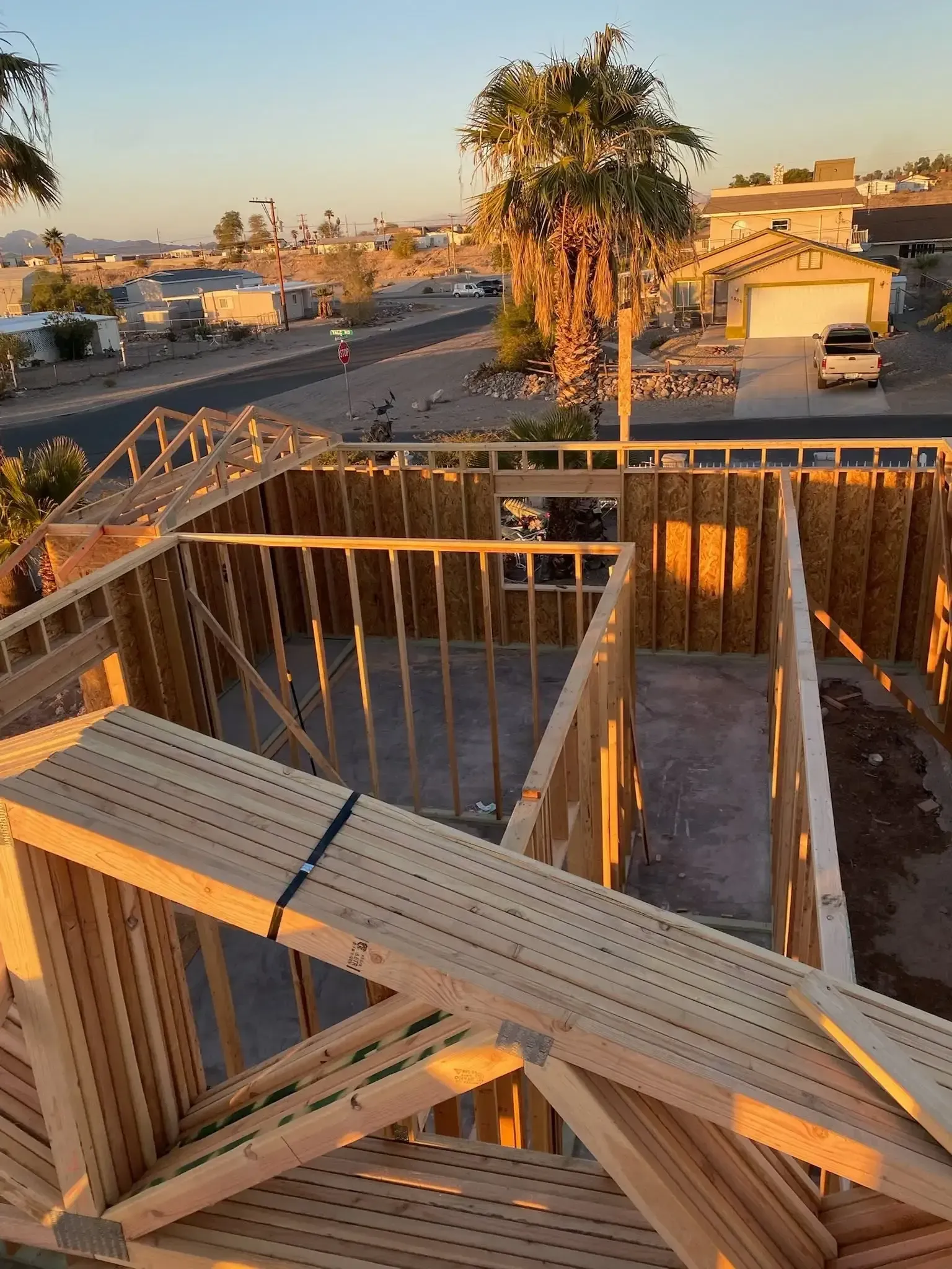 Sunset view from a wooden deck framing a street, palm trees, and buildings in a residential area
