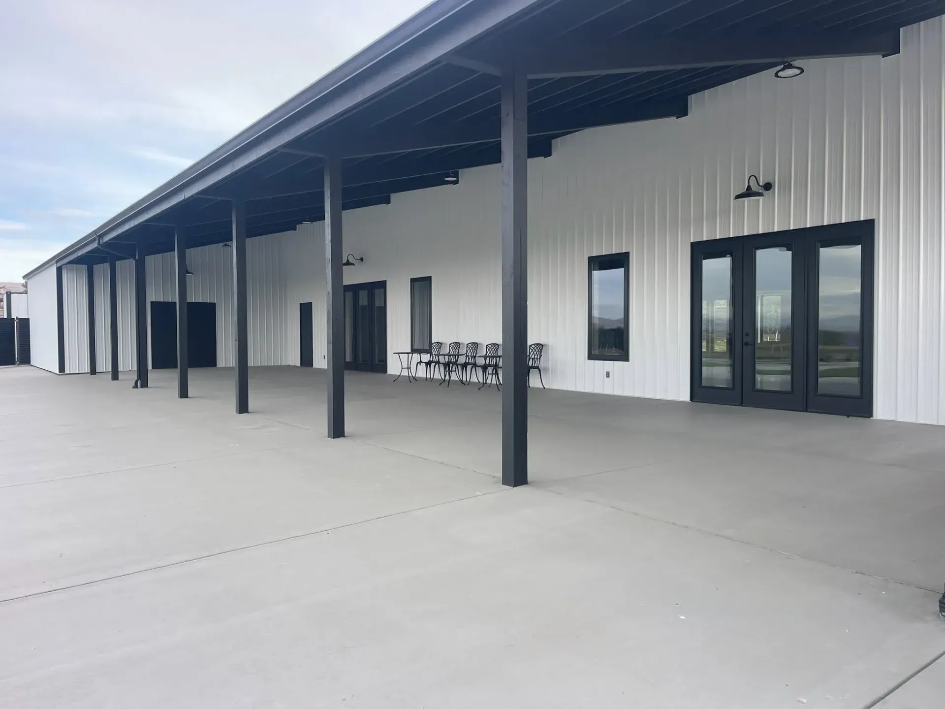Covered outdoor patio with white walls, black columns, and glass doors beside a concrete walkway.