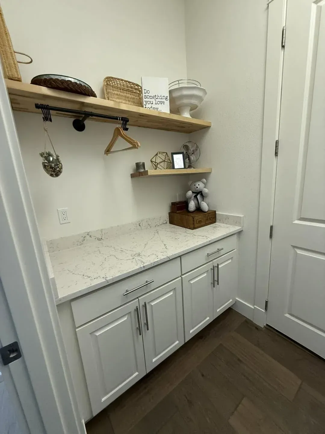 Small white cabinet with marble countertop, wall shelf decor, and hanging hooks in a narrow entryway.