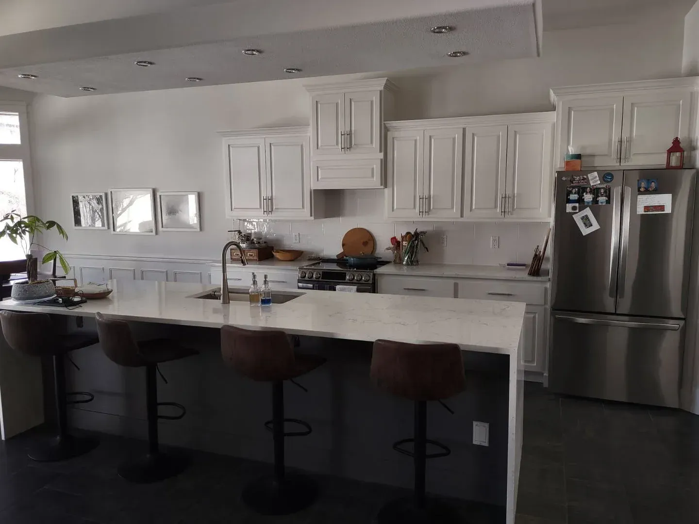 Modern white kitchen with island, three stools, and stainless steel refrigerator
