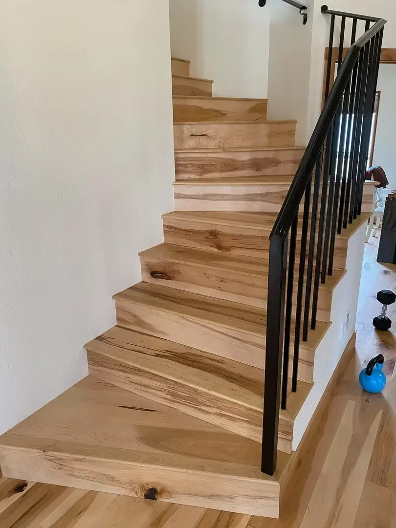 Wooden staircase with black railing and a small set of dumbbells on the floor beside it