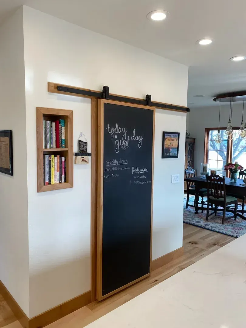 Tall black chalkboard wall sign in a bright home hallway with wood trim and nearby dining area.