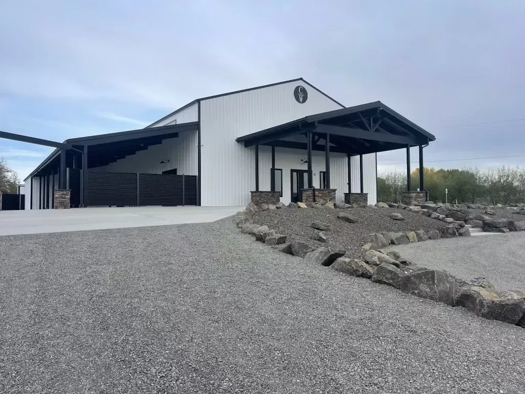 White metal industrial building with covered entrance on a gravel lot under a cloudy sky