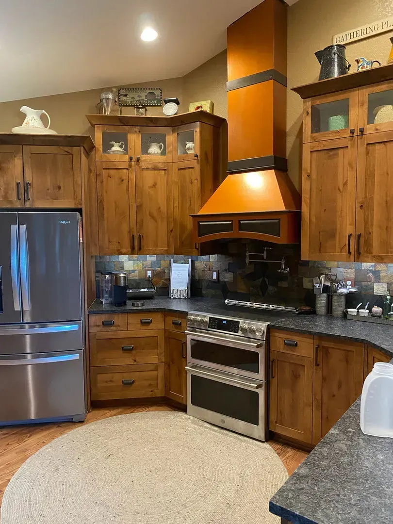 Wooden kitchen with stainless steel appliances, orange range hood, and granite countertops