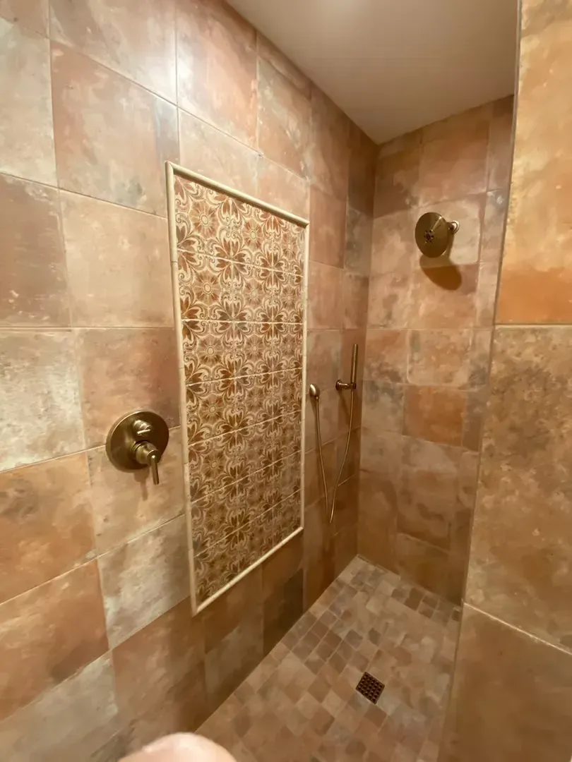 Tiled shower stall with a decorative accent panel and two bronze shower fixtures