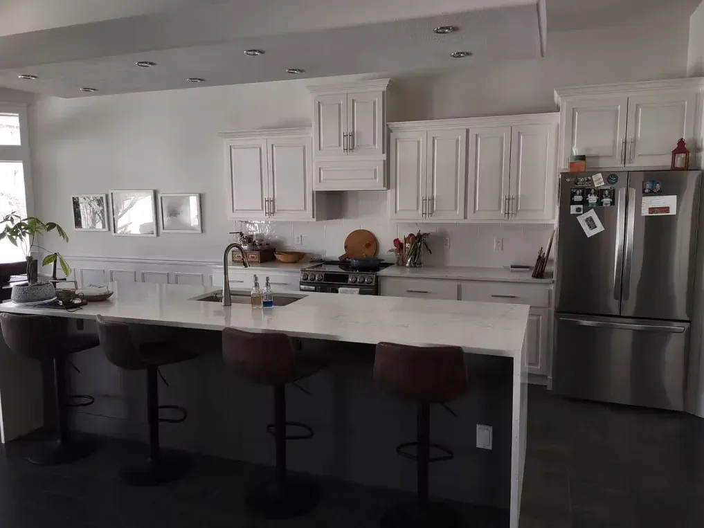 Modern white kitchen with island, bar stools, stainless steel fridge, and pendant lighting