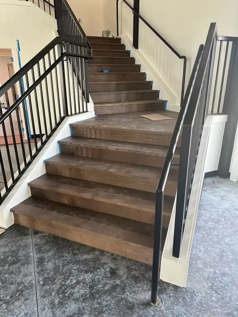 Brown carpeted staircase with black railings in a hallway