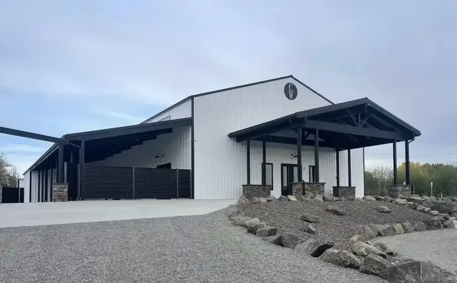 Modern white barn-style building with a black roof and gravel lot in a rural setting
