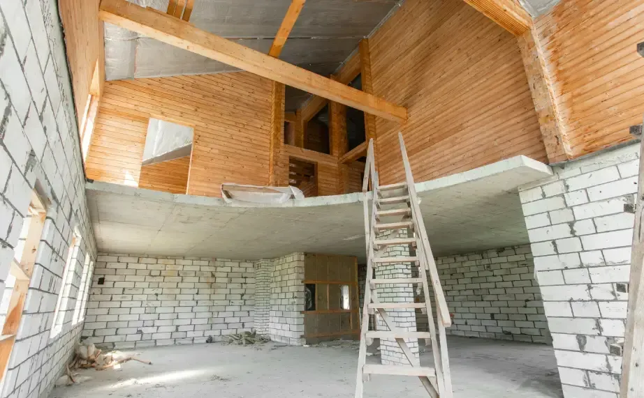 Partially built interior with brick walls, exposed wooden roof beams, and a ladder to a mezzanine platform