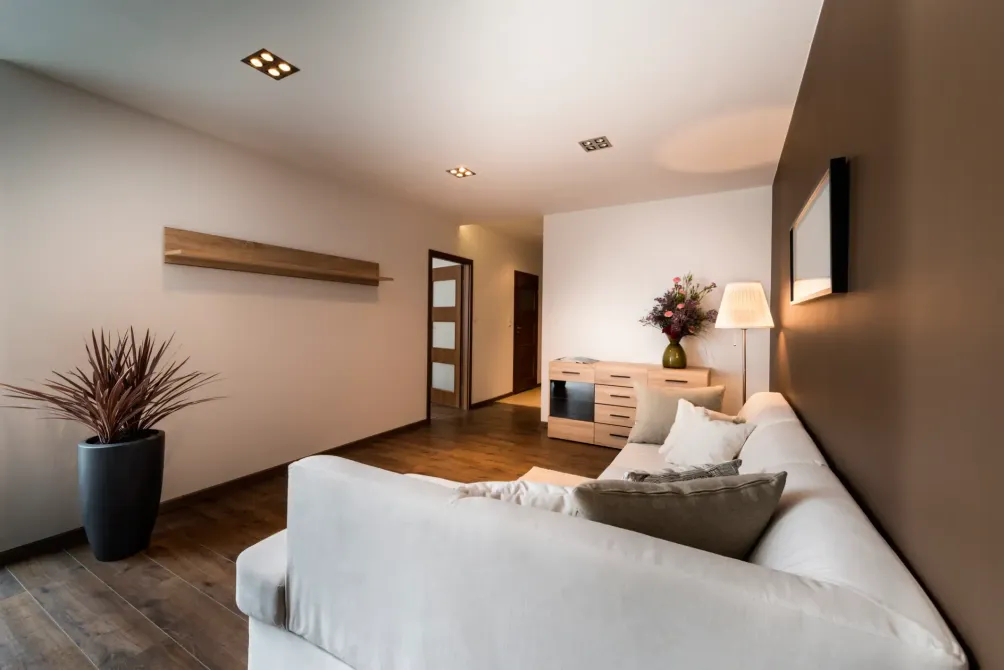 Modern minimalist living room with white sofa, wood flooring, wall shelf, and warm lighting