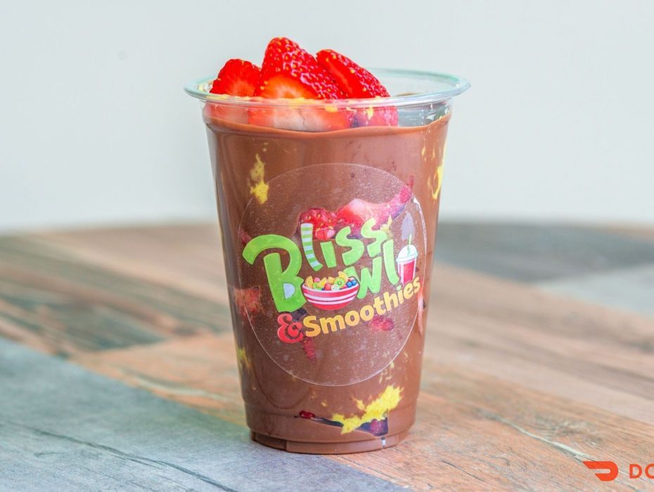 Strawberry smoothie in a clear plastic cup on a wooden table with colorful branding.