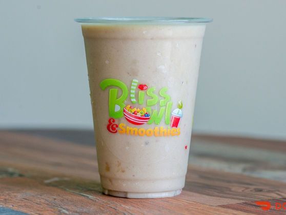 Blended smoothie in a clear plastic cup with a colorful “Bliss” logo on a wooden table