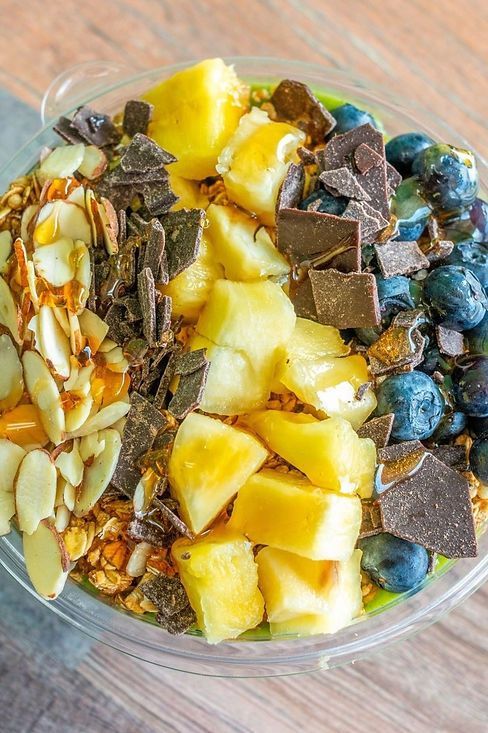 Glass bowl of chopped fruit, nuts, chocolate pieces, and blueberries on a wooden surface