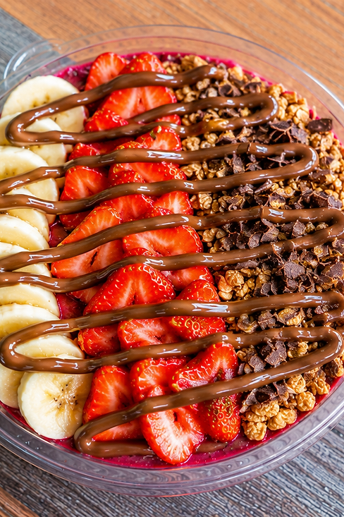Fruit and granola bowl drizzled with chocolate on a wooden table